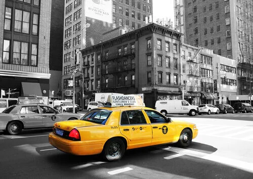 Fotorealistyczne zdjęcie żółtej taksówki marki Ford Crown Victoria na ruchliwej ulicy miasta. Taksówka ma żółte nadwozie i czarno-białą szachownicę.